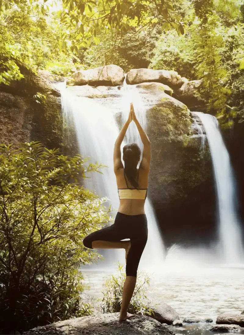 Fotografía de una mujer haciendo yoga en un paisaje natural con una cascada de fondo